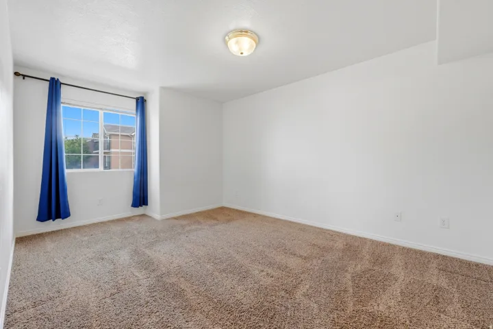 Carpeted interior room featuring a multi-pane window, white walls, and a ceiling-mounted light fixture