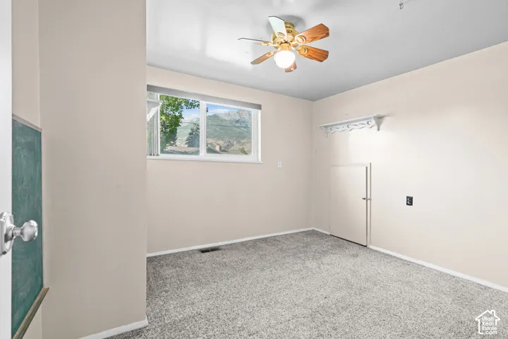 Carpeted room with a ceiling fan, a window offering mountain scenery, light-colored walls, and a built-in wall shelf