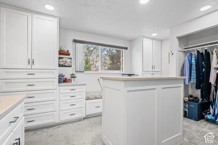 Spacious walk-in closet featuring white built-in cabinetry, a central island with a solid surface countertop, and recessed lighting