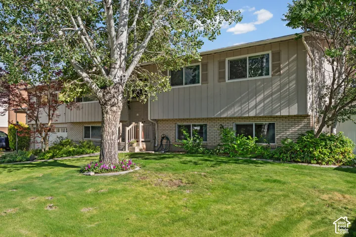 Split-level residence featuring a brick and vertical siding exterior, a front entry with wooden railings, and multiple mature trees