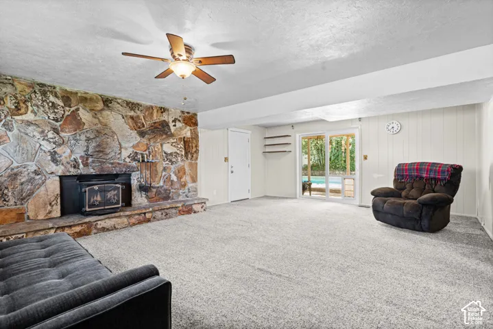 Spacious room featuring a stone-clad fireplace with an insert, light gray carpeting, and a ceiling fan