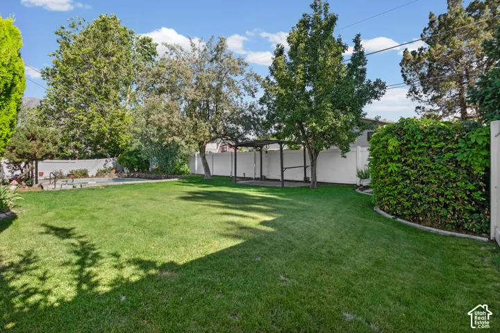 Expansive lawn area featuring a pergola structure, mature perimeter trees, and a white privacy fence