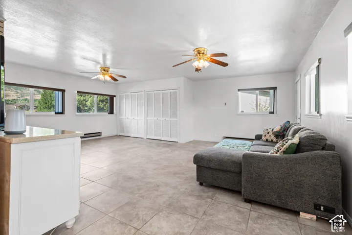 Spacious room featuring tile flooring, multiple windows providing natural light, and two ceiling fans with integrated lighting