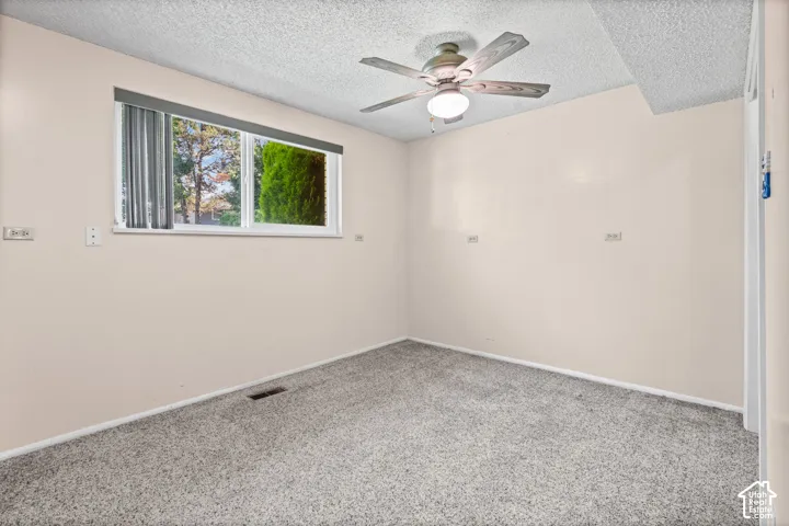Spacious room featuring neutral carpeting, a ceiling fan with integrated lighting, and a large window with vertical blinds