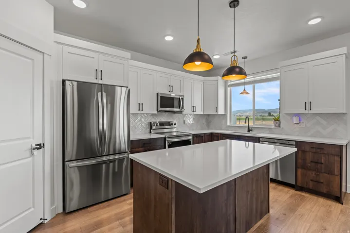 Modern kitchen featuring an expansive center island with a white countertop, two-tone cabinetry, stainless steel appliances, and wood-finish flooring
