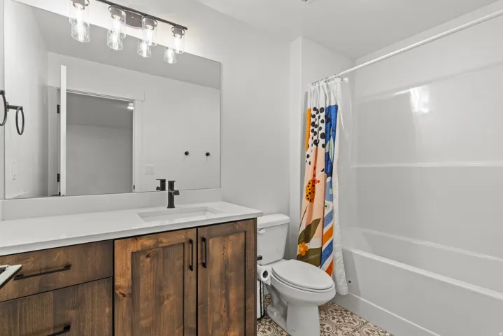 Bathroom featuring a wood-finish vanity with a white countertop and integrated sink, matte black hardware, a rectangular mirror, and a full bathtub with shower