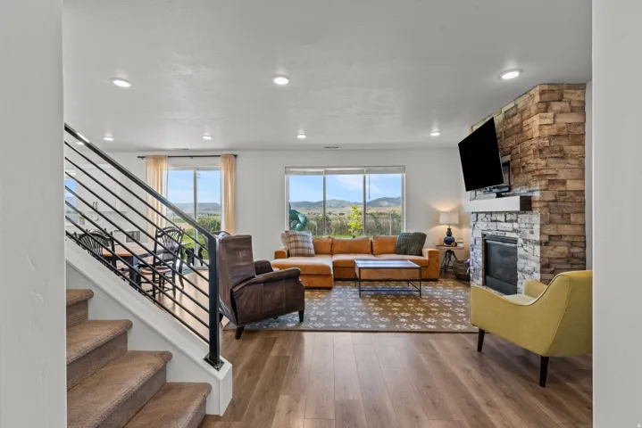 Open-concept living area featuring wood-finish flooring and a stone-clad fireplace with a white mantel