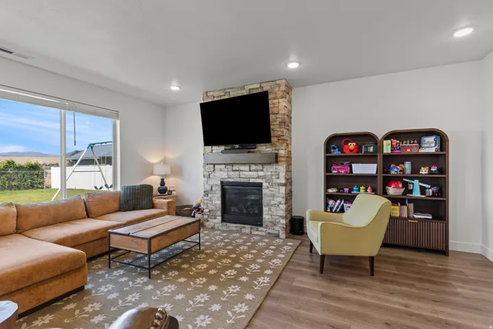Living area featuring a stone-clad fireplace with a wood mantel, a large picture window, recessed lighting, and wood-finish flooring