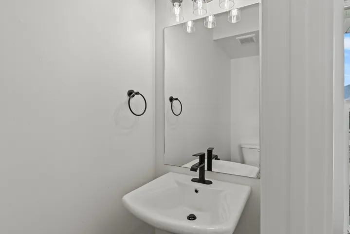 Pedestal sink with a matte black faucet, rectangular mirror, and three-light vanity fixture