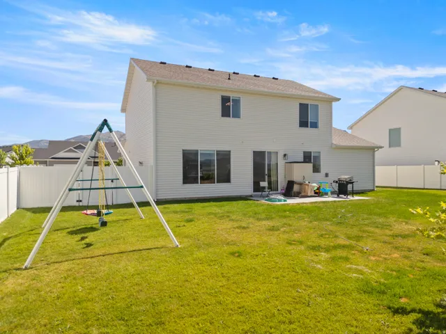 Spacious backyard featuring a large green lawn, a white vinyl fence, a concrete patio, and a two-story residence with white siding