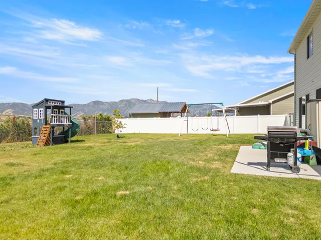 Expansive green lawn with a white vinyl fence, concrete patio, and a mountain range backdrop