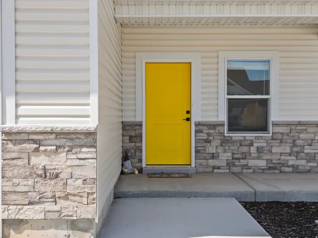 Inviting entry featuring a bright yellow door, concrete pathway, and a single-hung window
