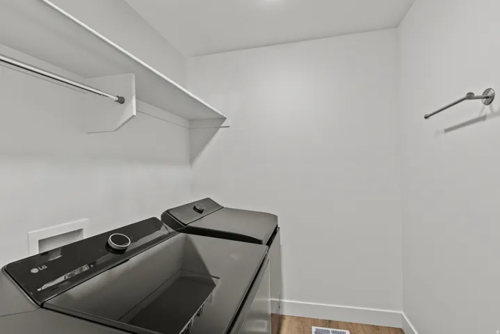 Dedicated laundry area featuring white walls, a built-in shelving unit, a hanging rod, a wall-mounted towel bar, and wood-finish flooring