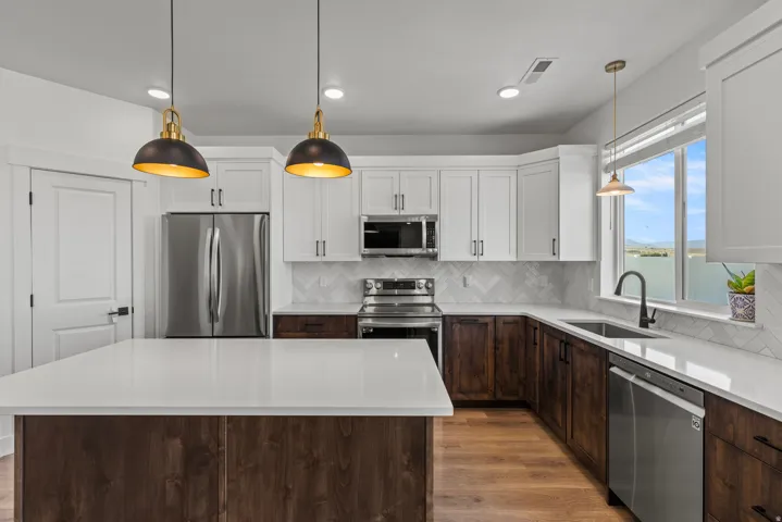 Spacious kitchen featuring a large island with a solid surface countertop, two-tone cabinetry, stainless steel appliances, and a herringbone tile backsplash