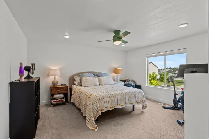 Recessed lighting, a ceiling fan, and a large window illuminate this carpeted room