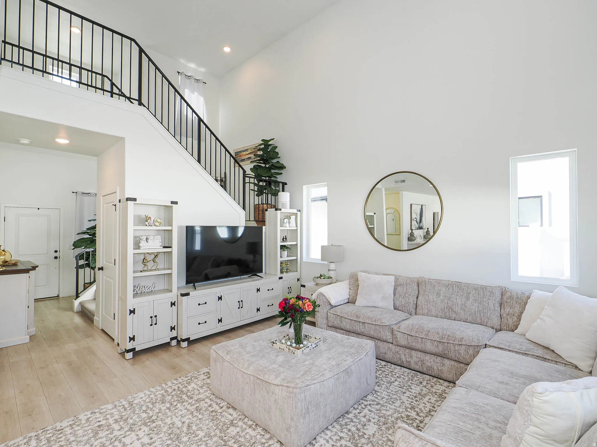 Great room featuring light wood-finish flooring, high vaulted ceilings, and a black metal spindle staircase