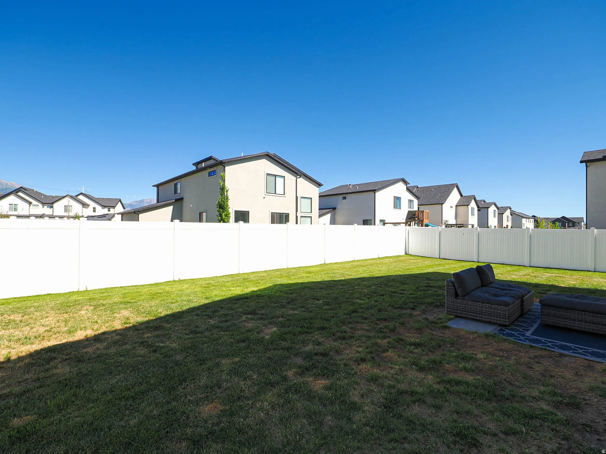 Spacious, enclosed backyard featuring a white vinyl fence and a green lawn