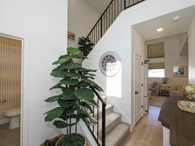 Two-story foyer with wood-finish flooring, a carpeted staircase with black iron railings, and a powder room featuring patterned wallpaper and a white toilet