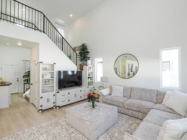 Great room featuring light wood-finish flooring, high vaulted ceilings, and a black metal spindle staircase