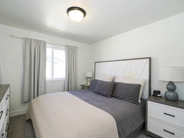 Carpeted bedroom featuring a window with natural light, a ceiling-mounted light fixture, and a decorative headboard