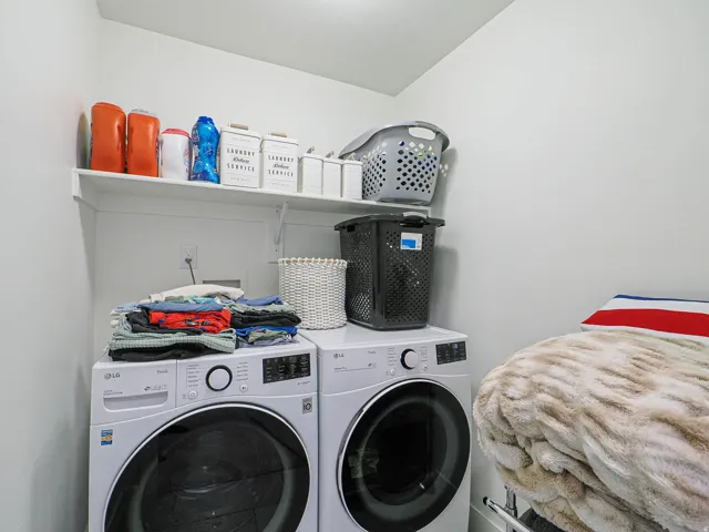 Dedicated laundry area featuring a white wall shelf, built-in wall outlet, and light-colored walls