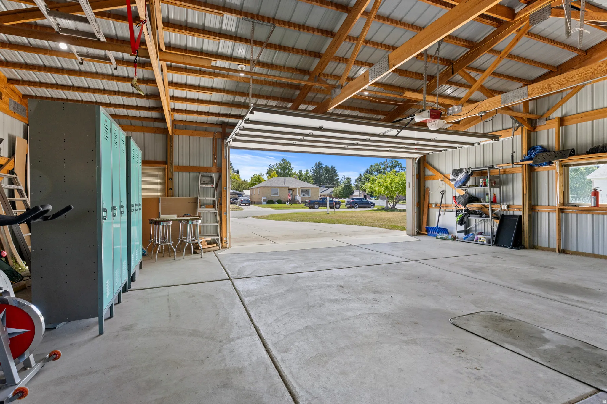 Spacious outbuilding featuring a corrugated metal roof and walls, exposed wood beam construction, concrete flooring, and an overhead garage door