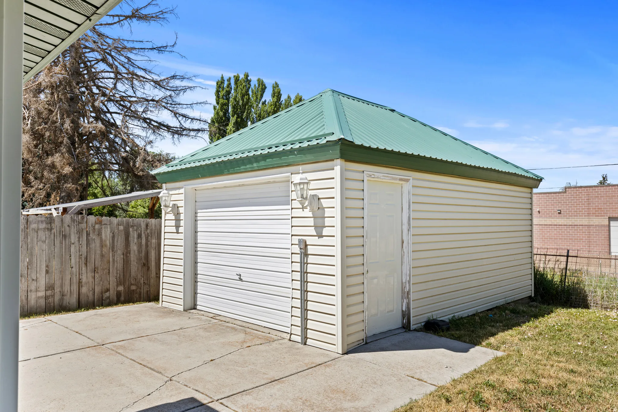 Detached garage with a green metal roof, light-colored siding, and a single garage door