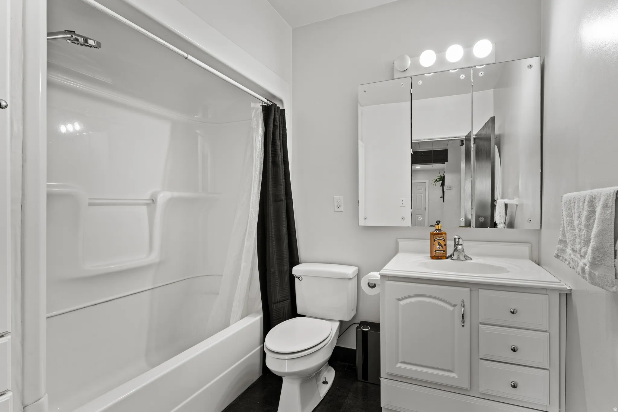 Bathroom featuring a white bathtub/shower combination, a white vanity with an integrated sink, a mirrored medicine cabinet, and a three-bulb light fixture