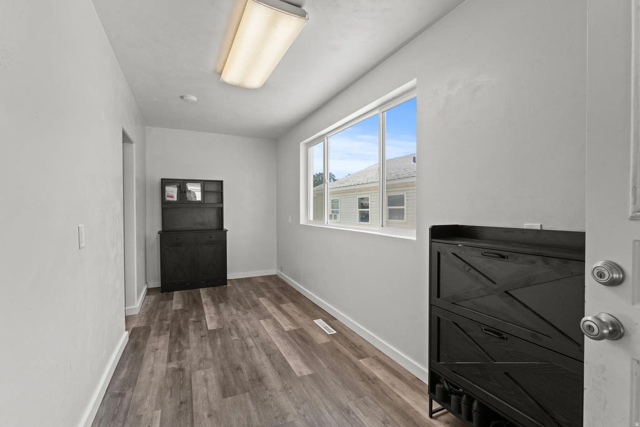 Interior room featuring wood-finish flooring, white baseboards, and a large window providing natural illumination