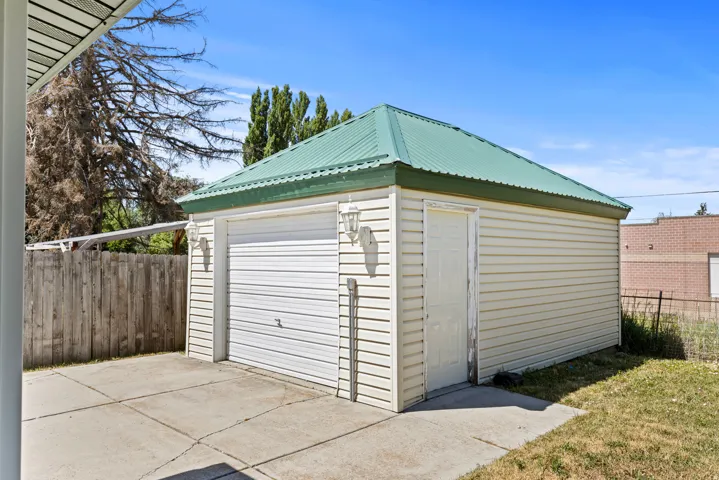 Detached garage with a green metal roof, light-colored siding, and a single garage door