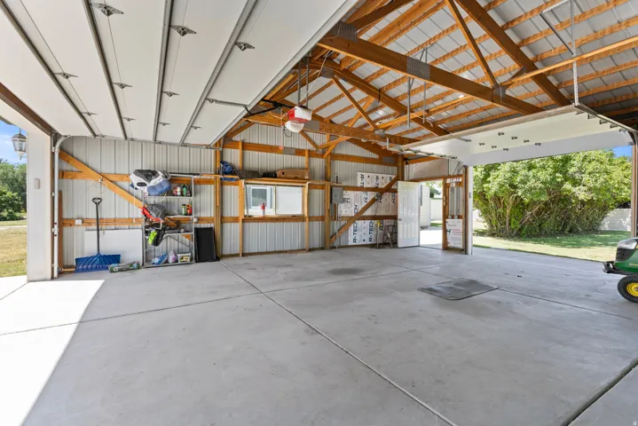 Spacious garage featuring a concrete floor, exposed wood beam ceiling, metal siding, and an overhead garage door