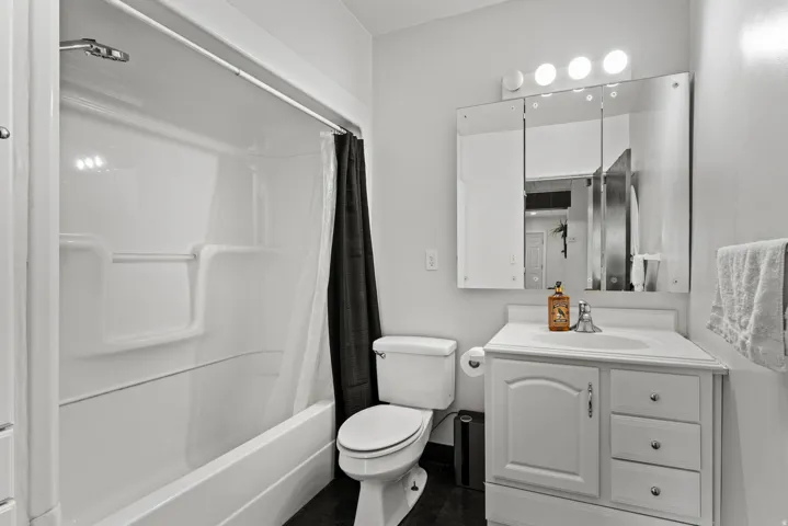 Bathroom featuring a white bathtub/shower combination, a white vanity with an integrated sink, a mirrored medicine cabinet, and a three-bulb light fixture