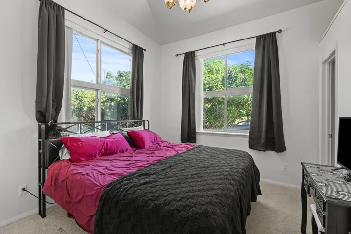 Bright bedroom featuring two large windows, a vaulted ceiling, recessed lighting, and light-toned carpeting
