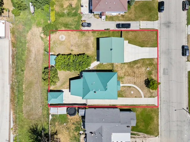 Aerial view showcasing the property's perimeter, a main residence with a green roof, a detached garage with a green roof, a separate accessory structure with a green roof, concrete driveways, and a circular concrete walkway