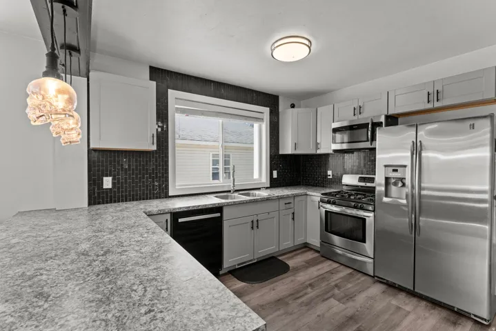 Contemporary kitchen featuring gray cabinetry, stainless steel appliances, dark subway tile backsplash, light-toned countertops, and wood-finish flooring