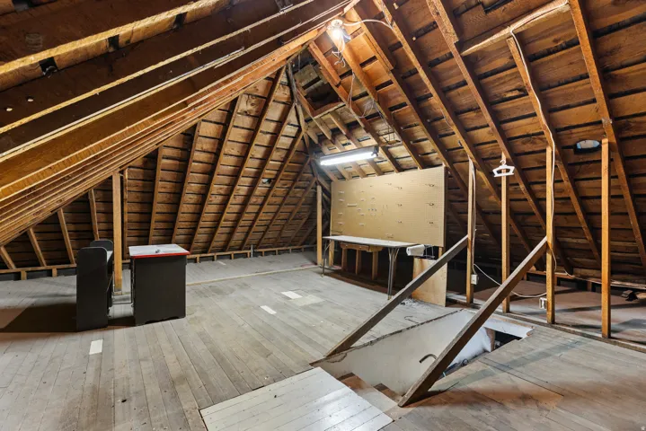 Spacious unfinished attic space featuring exposed wood rafter framing, wood flooring, and a built-in workbench