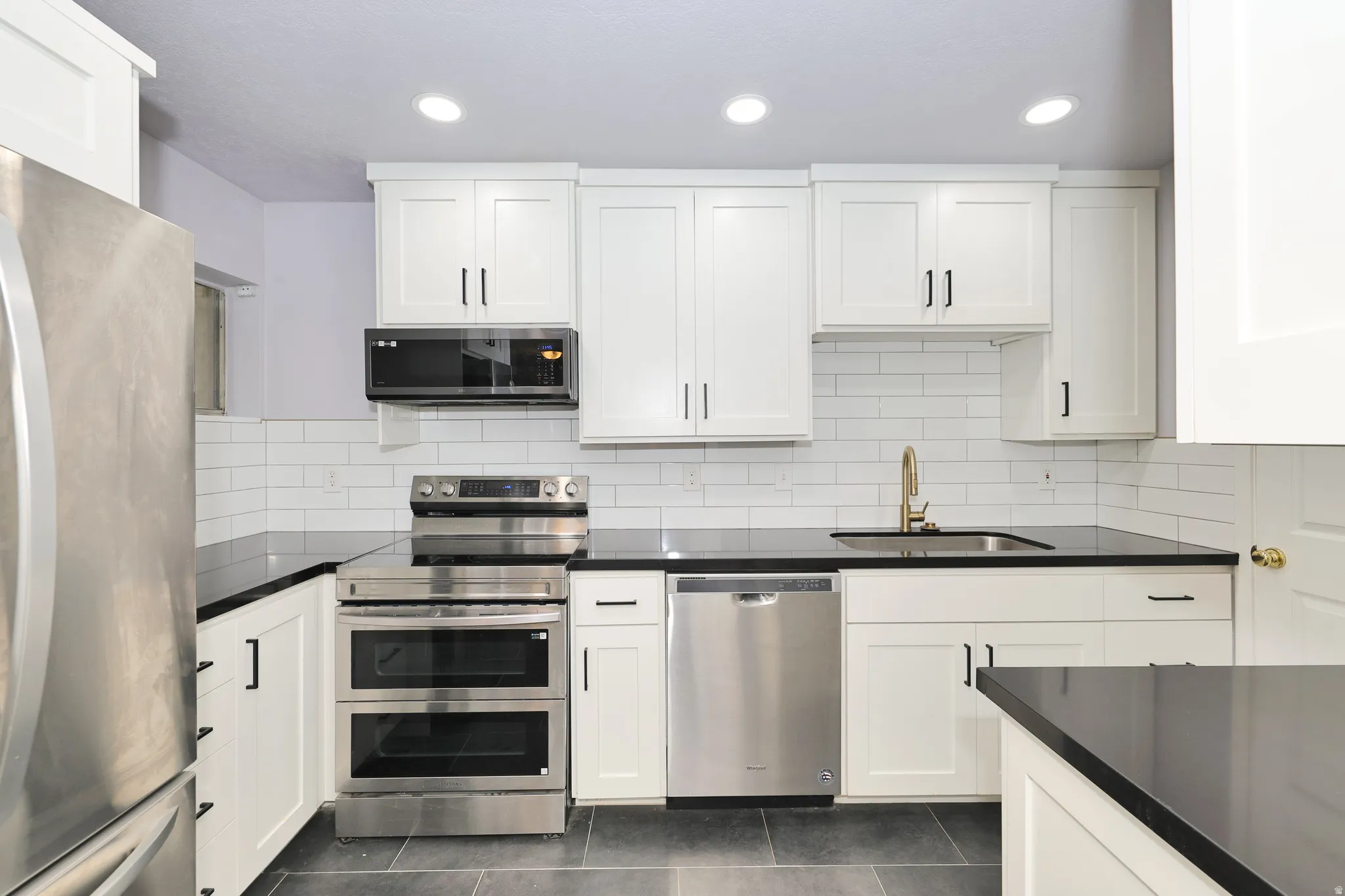 Modern kitchen featuring white shaker cabinetry, dark countertops, stainless steel appliances, a subway tile backsplash, and recessed lighting