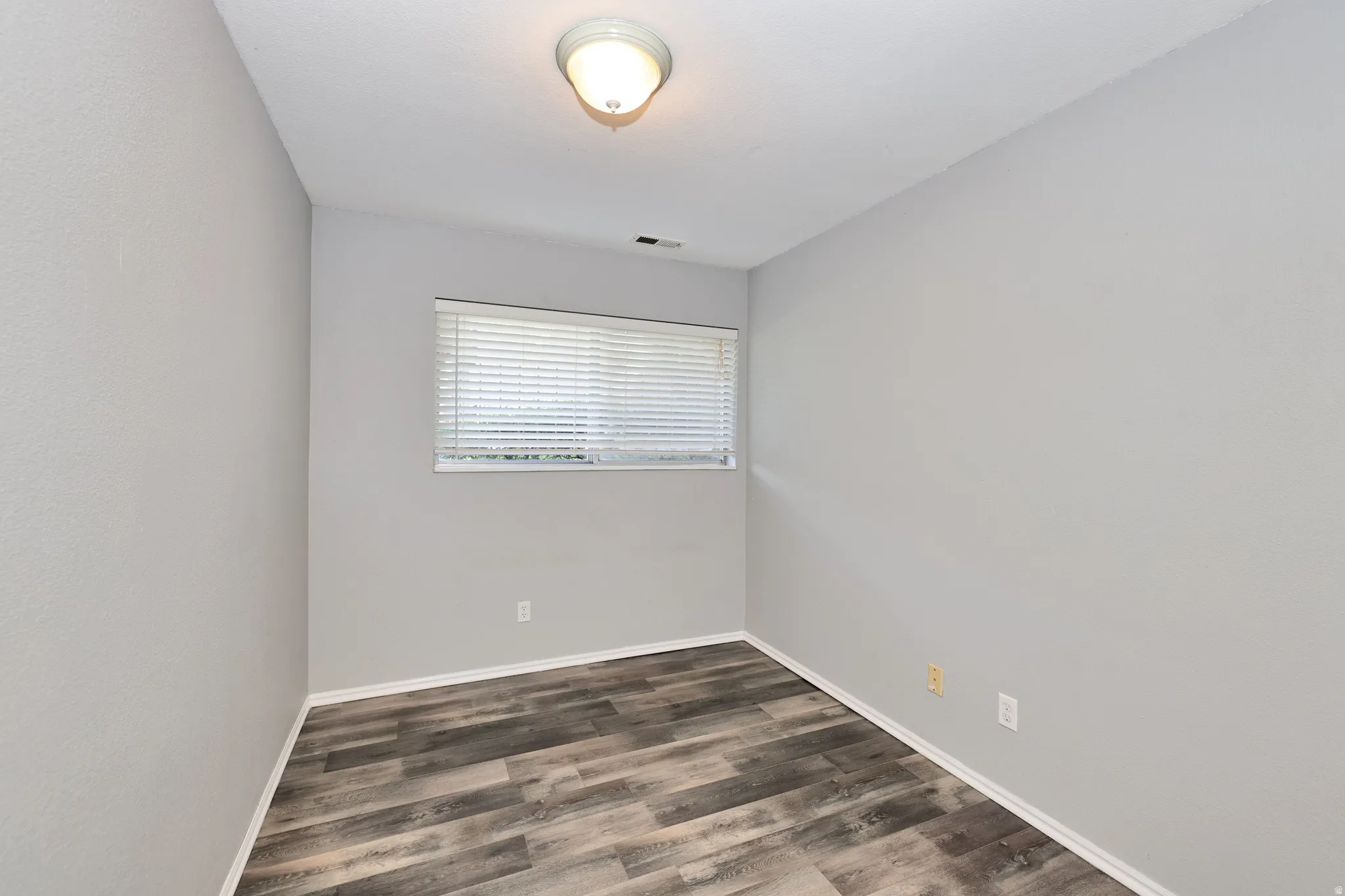Room featuring wood-finish flooring, light grey painted walls, and a window with blinds