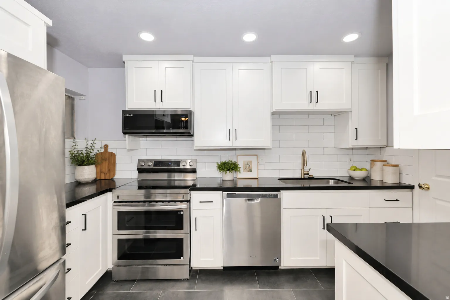Modern kitchen featuring white shaker cabinetry with dark hardware, dark countertops, a white subway tile backsplash, stainless steel appliances, and dark tile flooring