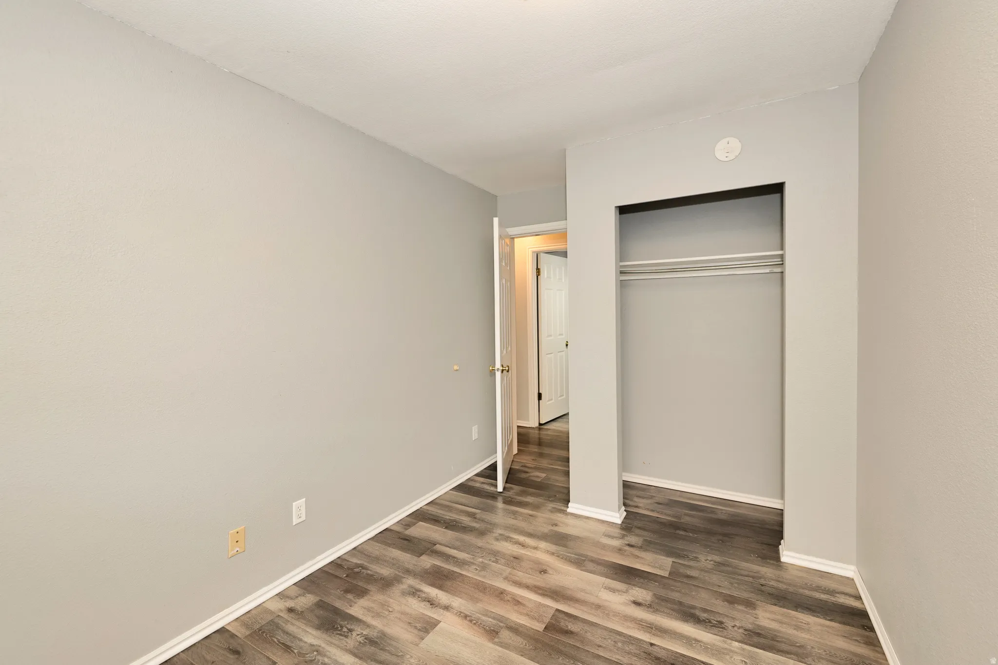 Room with wood-finish flooring, light gray painted walls, and white baseboards
