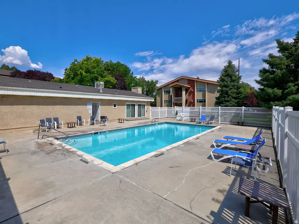 Rectangular swimming pool with a concrete surround, enclosed by a white privacy fence