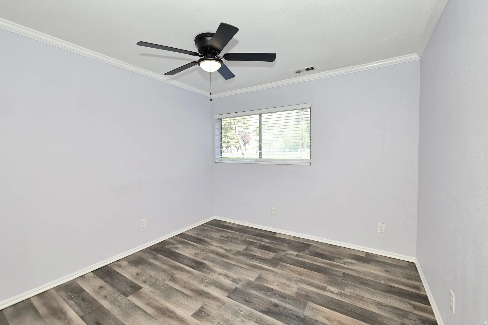 Room featuring wood-finish flooring, light purple wall paint, white crown molding, and a black ceiling fan with integrated lighting