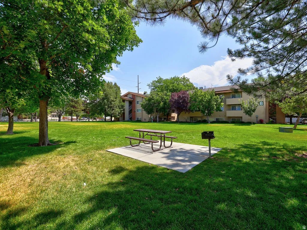 Expansive green space featuring a picnic table on a concrete pad, a built-in barbecue grill, and mature shade trees