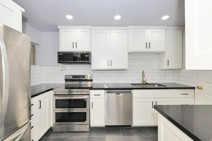 Modern kitchen featuring white shaker cabinetry, dark countertops, stainless steel appliances, a subway tile backsplash, and recessed lighting