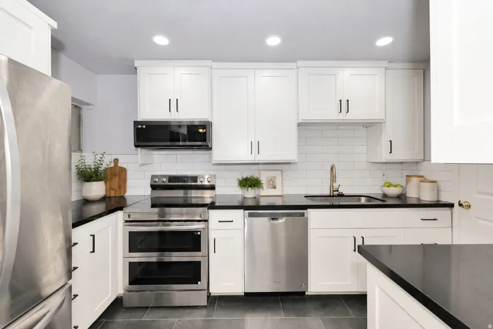Modern kitchen featuring white shaker cabinetry with dark hardware, dark countertops, a white subway tile backsplash, stainless steel appliances, and dark tile flooring