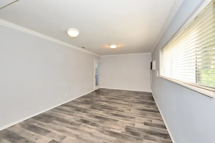Spacious room featuring wood-finish flooring, light gray walls, white crown molding, and two ceiling-mounted dome lights