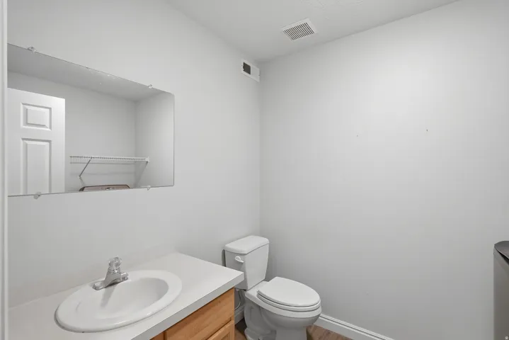 Compact half bath featuring a wood-finish vanity with an oval sink, ceramic tile flooring, and a low-profile toilet