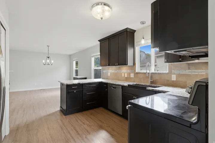 Kitchen featuring dark cabinetry, speckled countertops, a built-in dishwasher, stainless steel sink, and a tiled backsplash