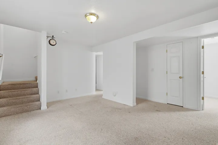 Spacious finished basement with neutral carpet flooring, multiple white interior doors, recessed ceiling lighting, and abundant natural light from windows