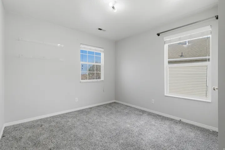 Bright secondary bedroom featuring neutral carpeting, dual windows with natural light, and fresh white walls with electrical outlets throughout